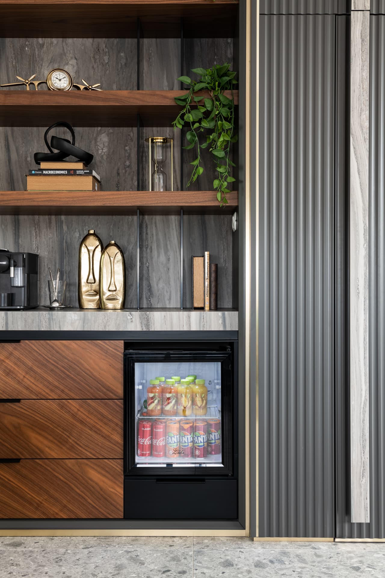 Walnut drawers and a glass-front mini fridge under stone-backed shelves with brass face sculptures in the executive office