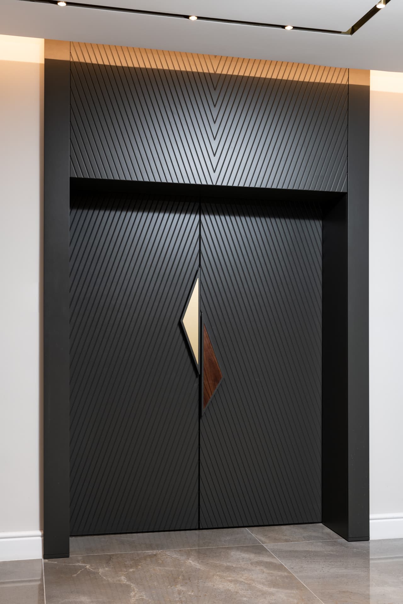 Matte black double entry doors with diagonal grooves and a split brass and walnut diamond handle at the office entrance
