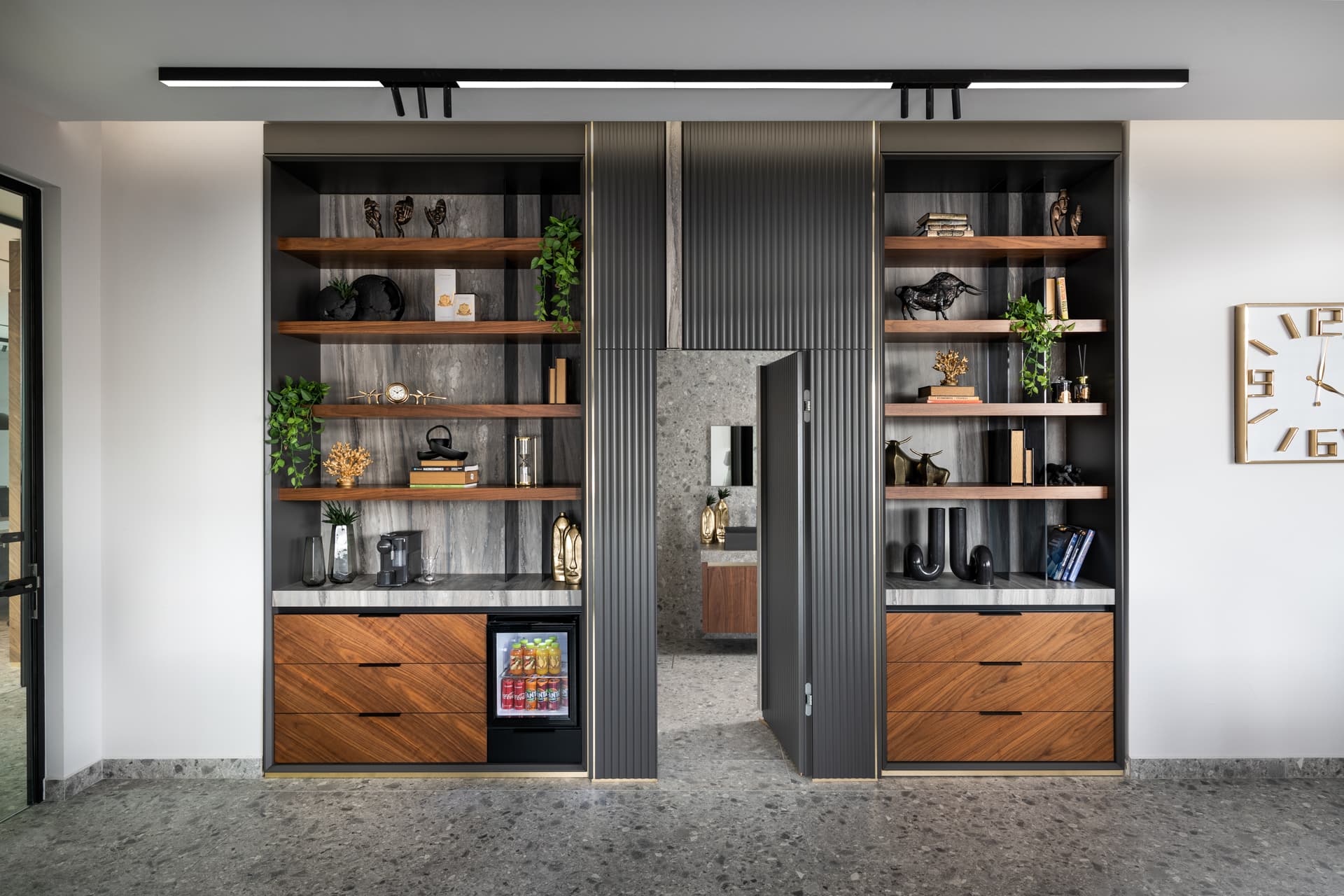 Walnut and stone display shelving framing a fluted charcoal hidden door that opens to a stone-clad room in the executive office