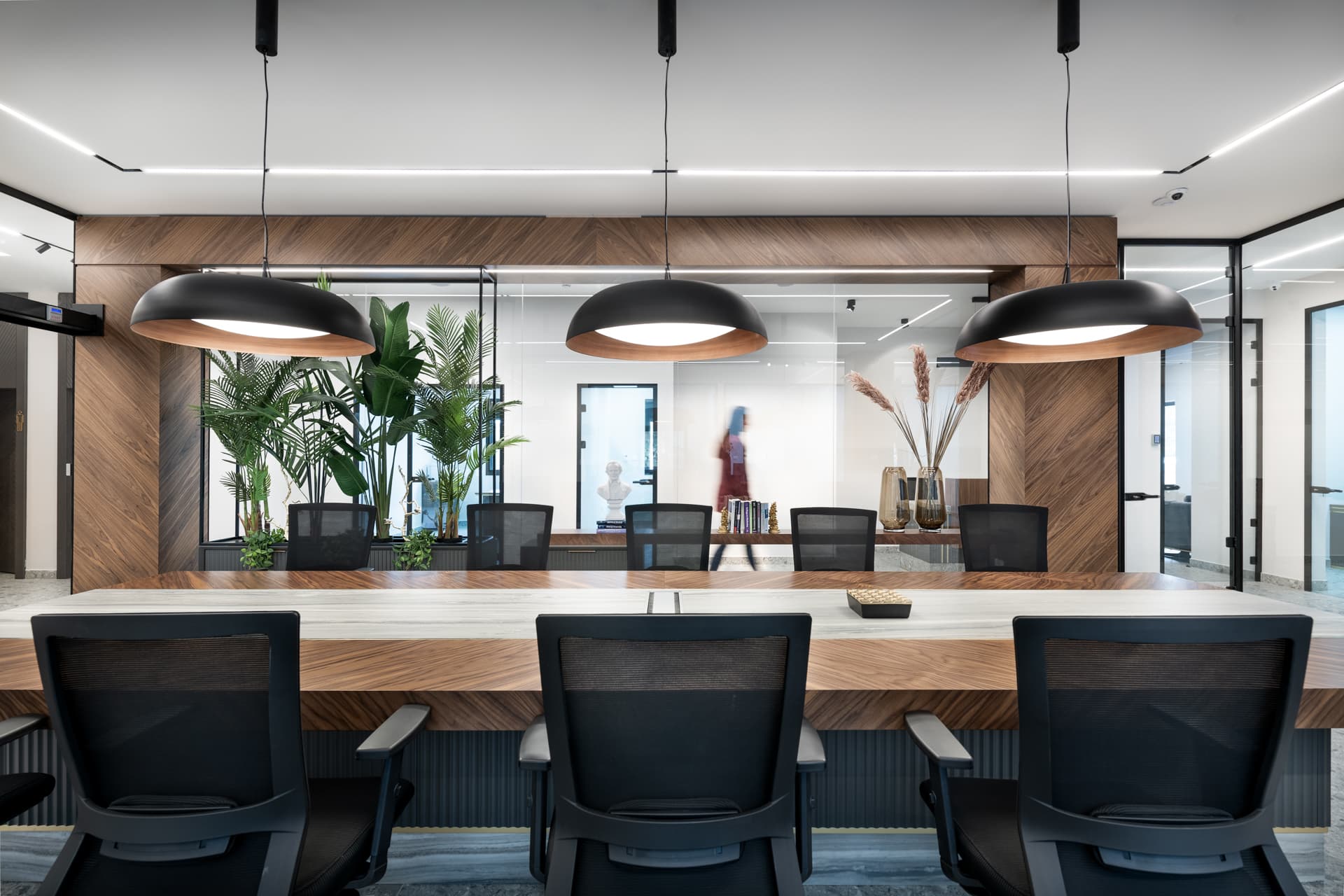 Shared walnut and veined stone work table with black mesh chairs under three large dome pendants in the office open workspace
