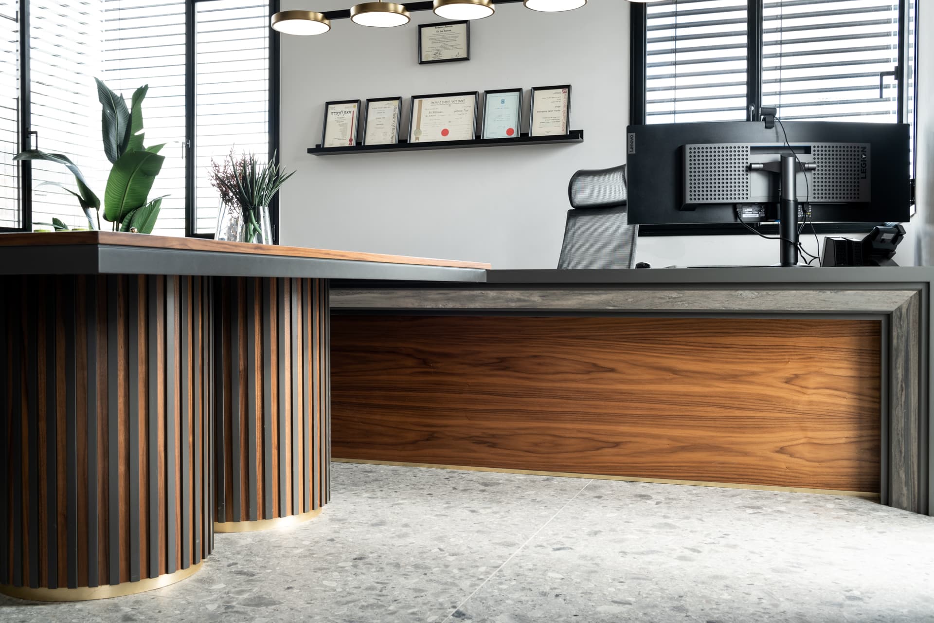 Low view of fluted walnut drum table bases meeting a stone-topped desk with a walnut front under brass disc pendants in the office