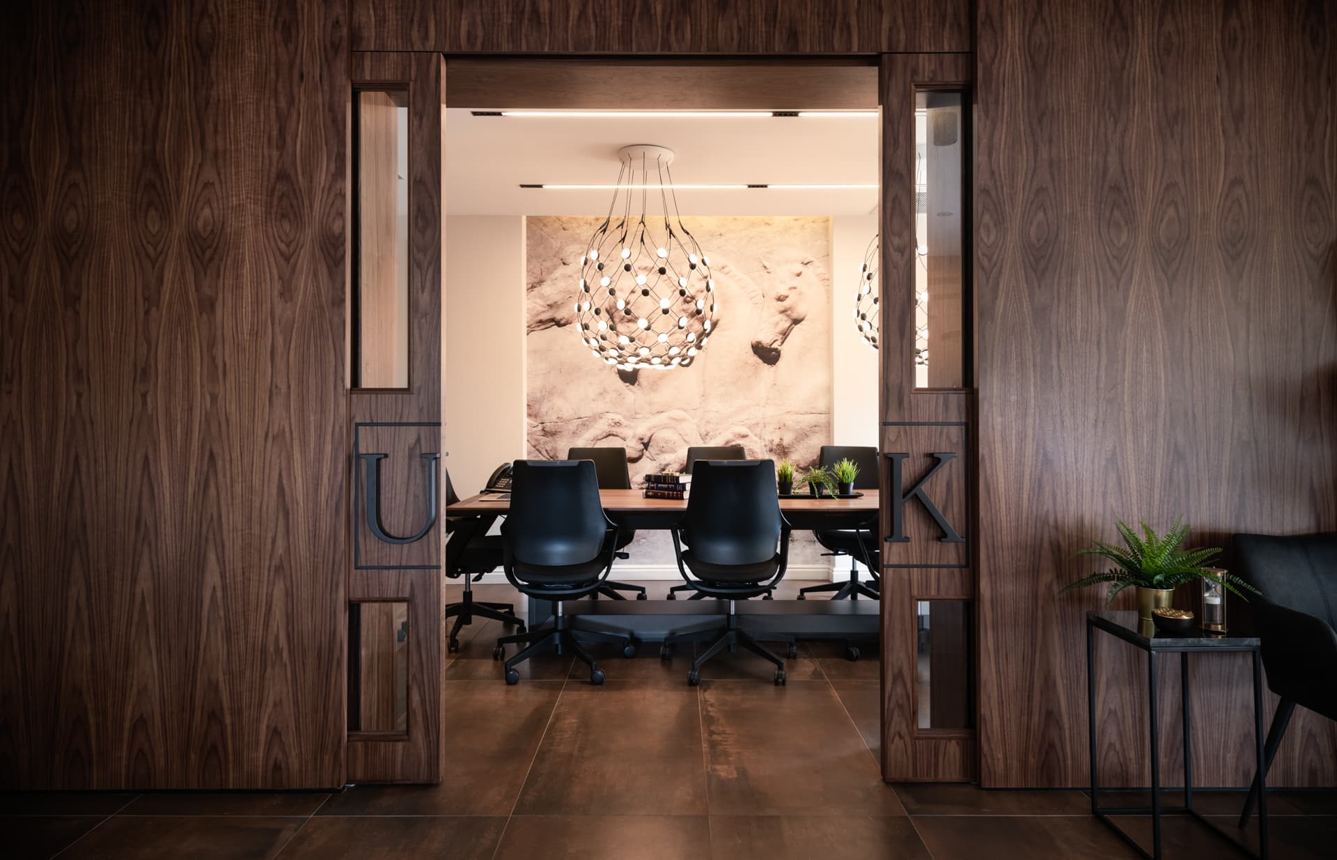 Open walnut sliding doors framing a meeting table under a globe pendant and a stone relief mural in the conference room of Othman Office 2