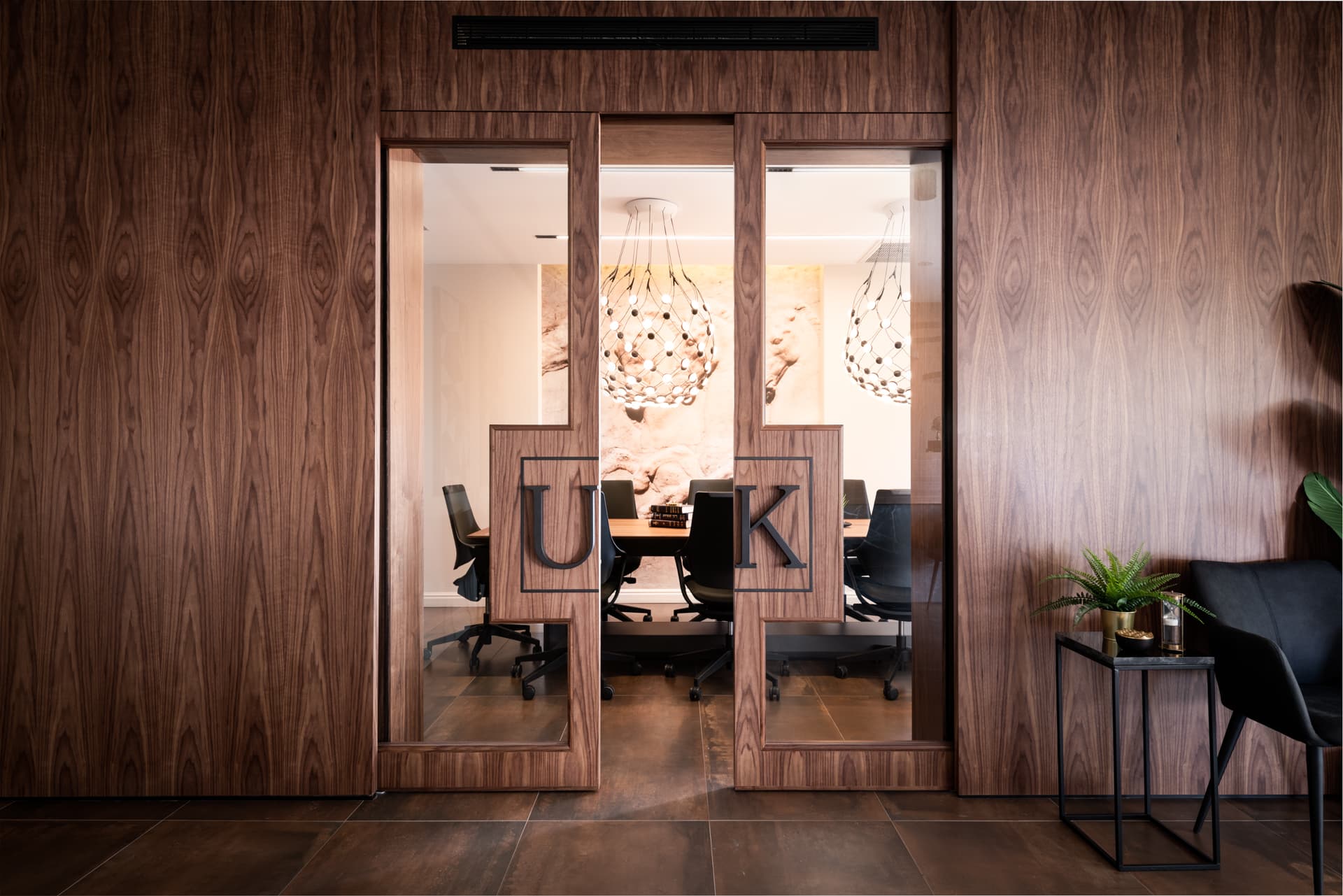 Closed walnut and glass sliding doors revealing the meeting table and globe pendants of the conference room of Othman Office 2