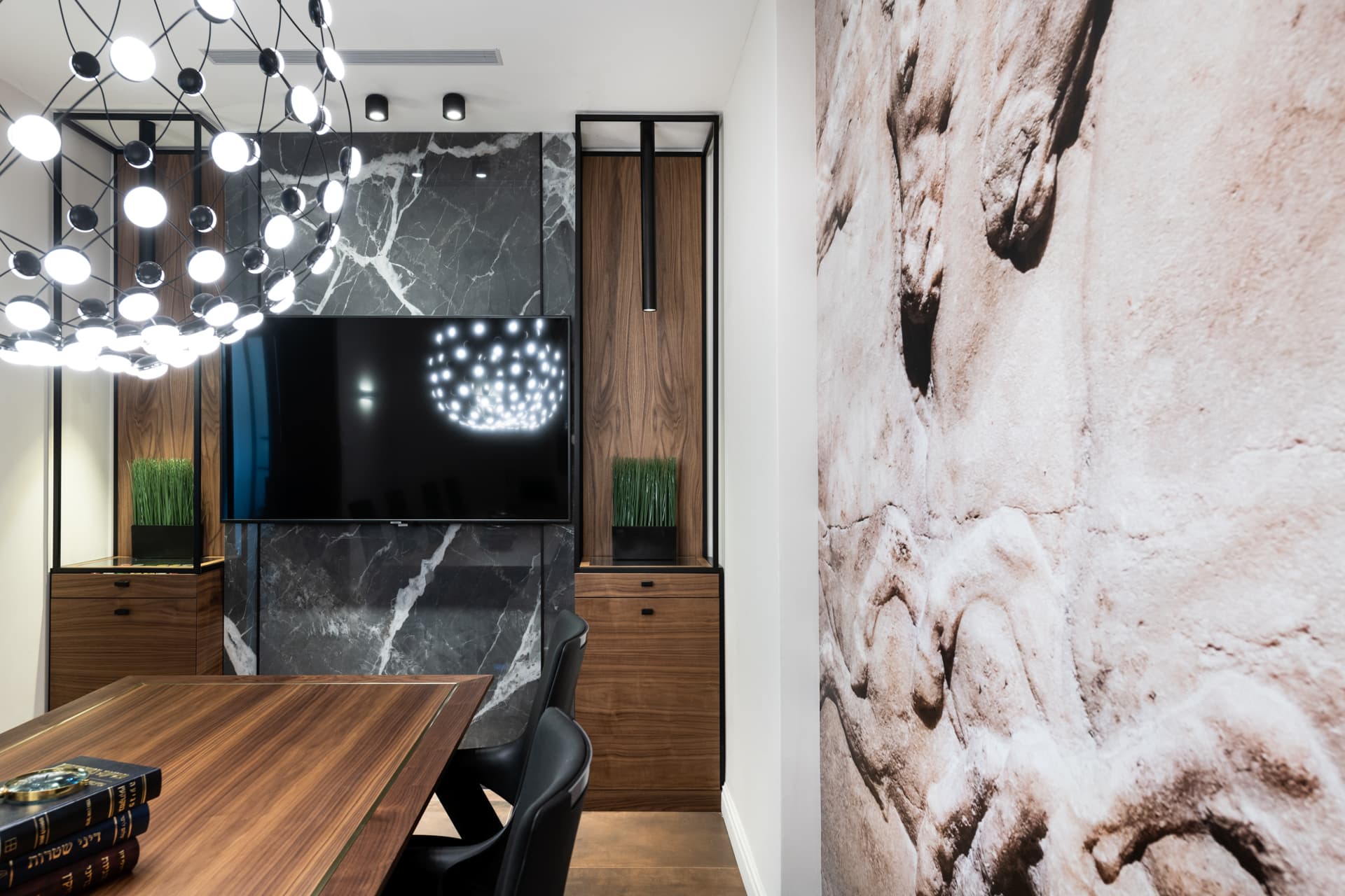 Dark veined stone media wall flanked by lit walnut display niches beside a carved relief mural in the conference room of Othman Office 2