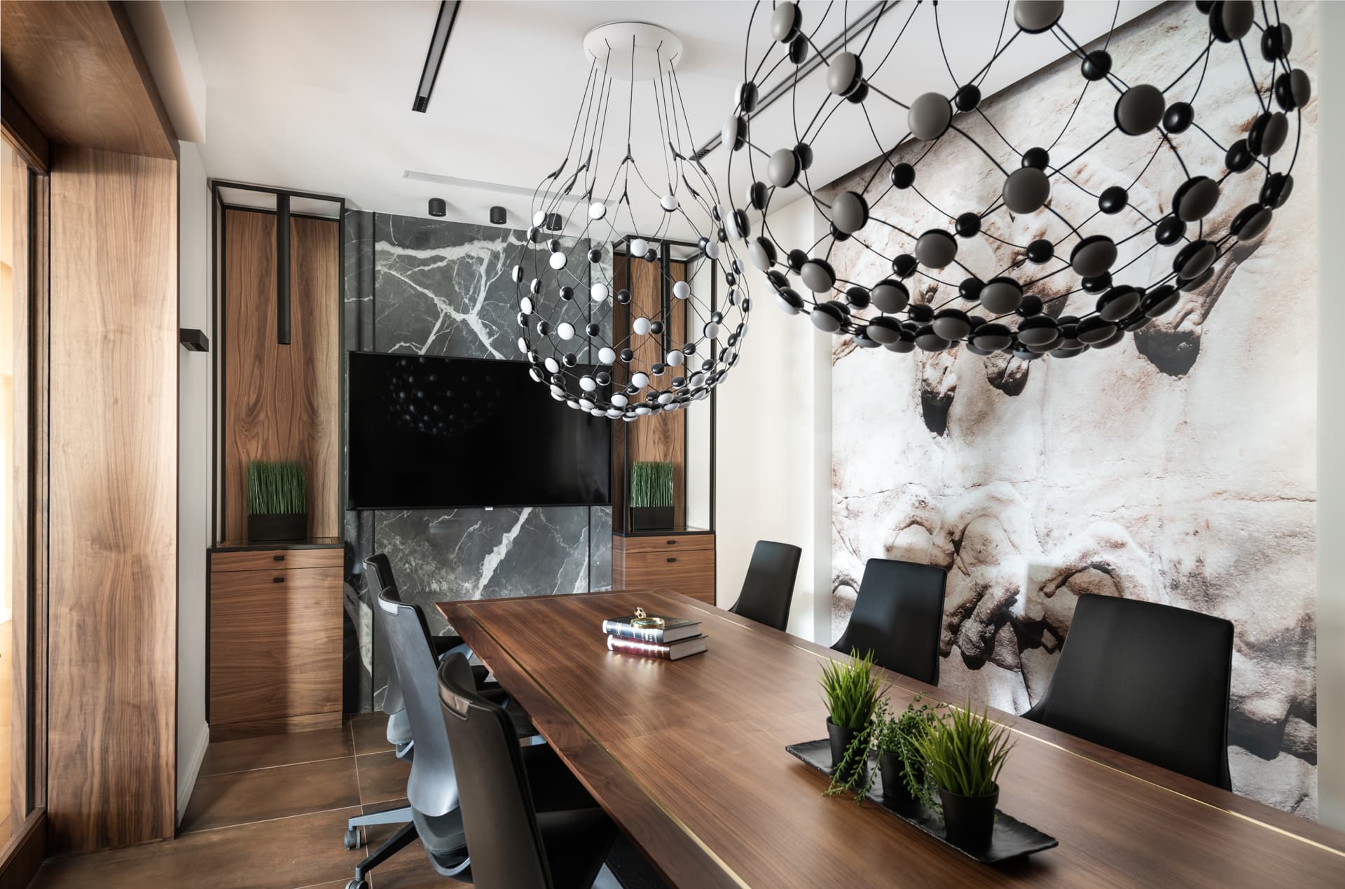 Long walnut meeting table beneath two dotted globe chandeliers against a stone relief mural in the conference room of Othman Office 2