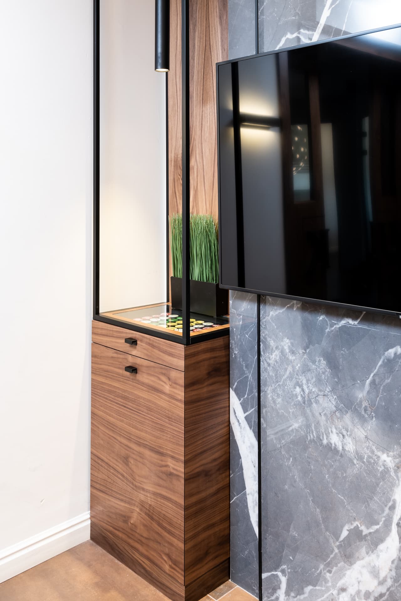 Walnut cabinet with a lit steel-framed niche beside a TV on a dark veined stone wall in the conference room of Othman Office 2