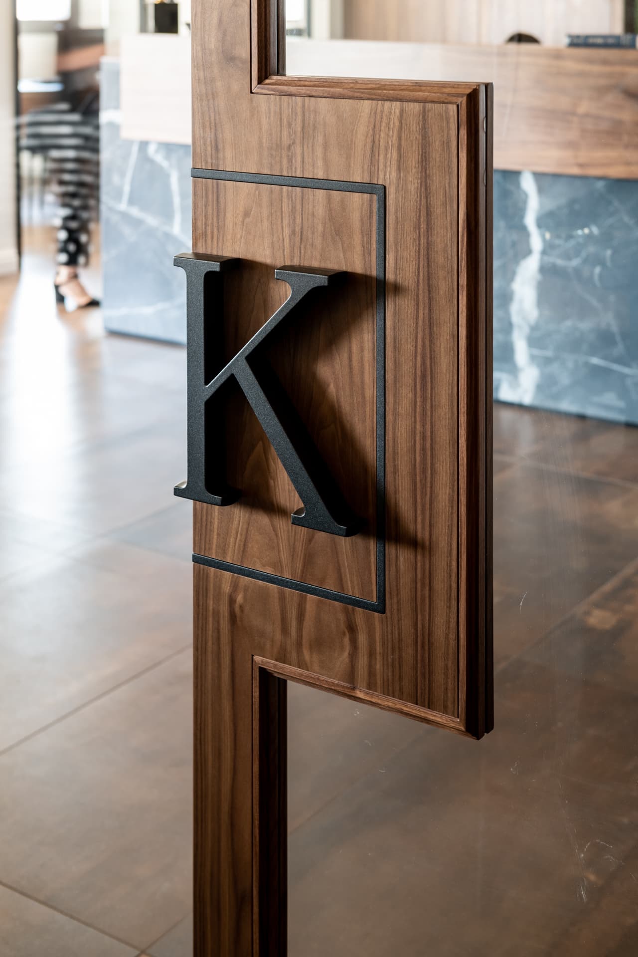 Raised black metal letter mounted on a framed walnut sliding door panel with glass inserts in the reception of Othman Office 2