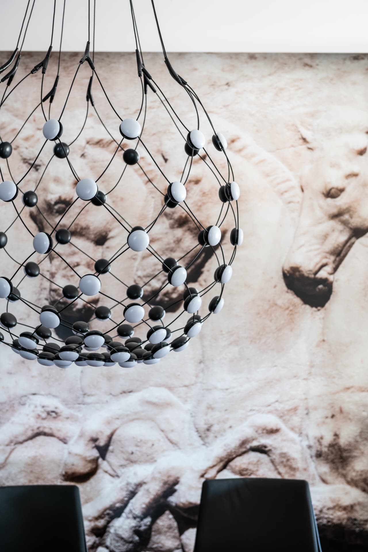 Globe chandelier of black and white dotted lights hanging before a carved stone relief mural in the conference room of Othman Office 2