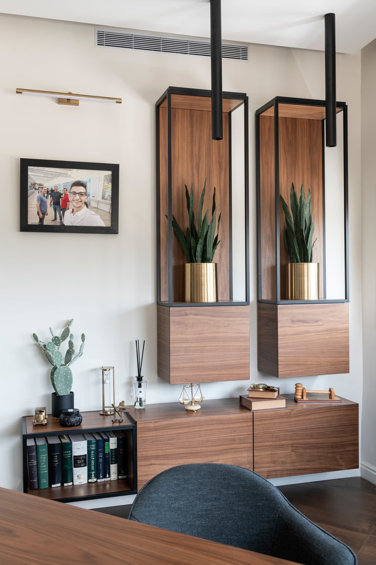Suspended walnut boxes in black steel frames with brass-potted snake plants over a low credenza in the private office of Othman Office 2