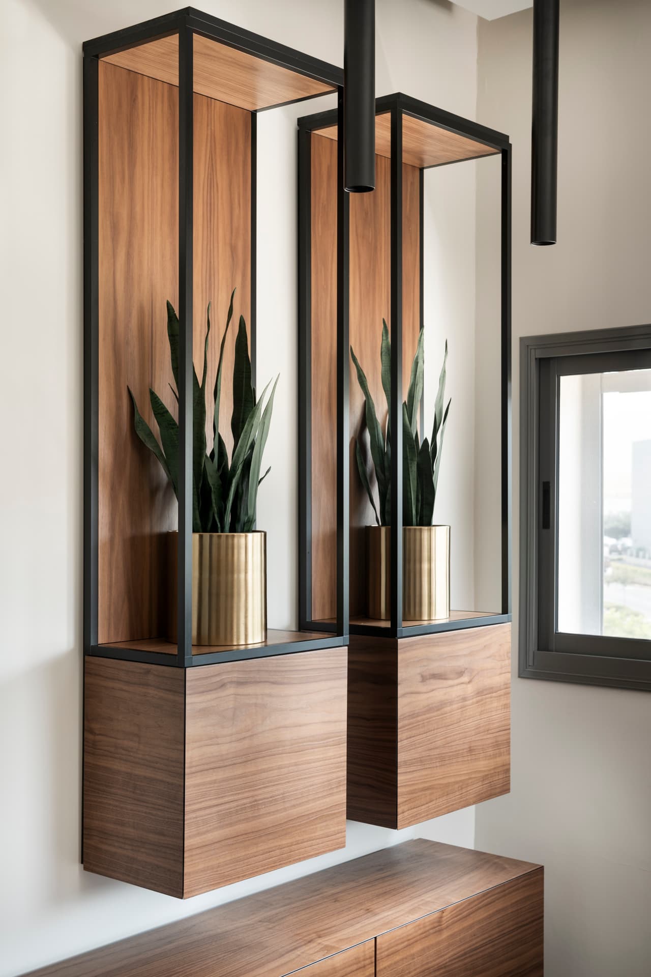 Two floating steel-framed walnut niches with snake plants in ribbed brass planters beside a window in the private office of Othman Office 2