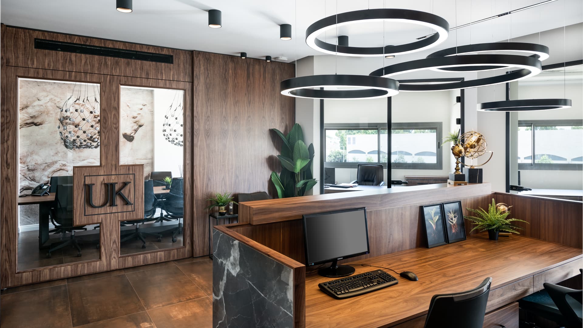 Walnut workstation counter with a stone-clad end beside the glass-fronted meeting room in the open office of Othman Office 2