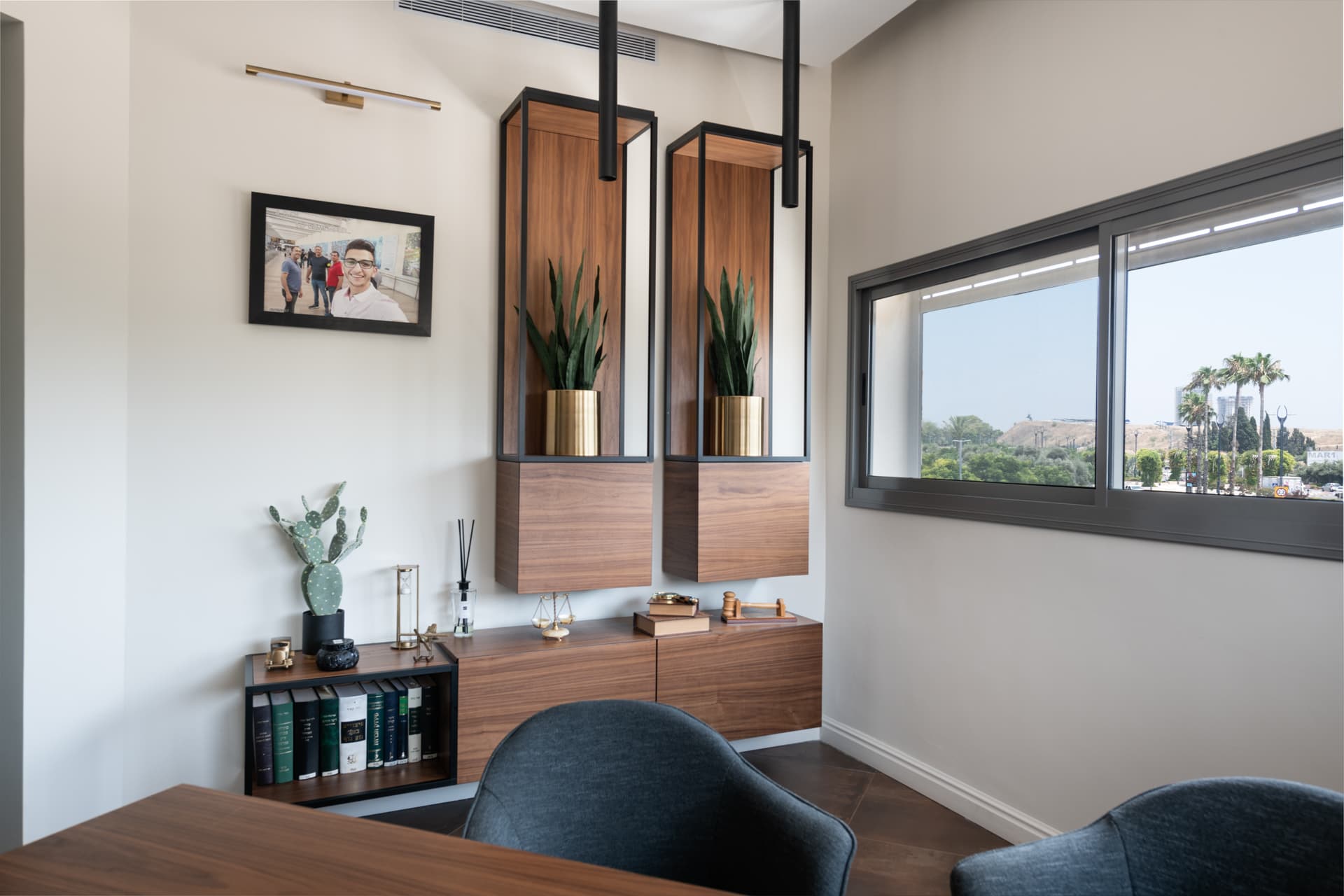 Floating walnut cabinets with steel-framed planter niches and a low bookshelf beside a wide window in the private office of Othman Office 2