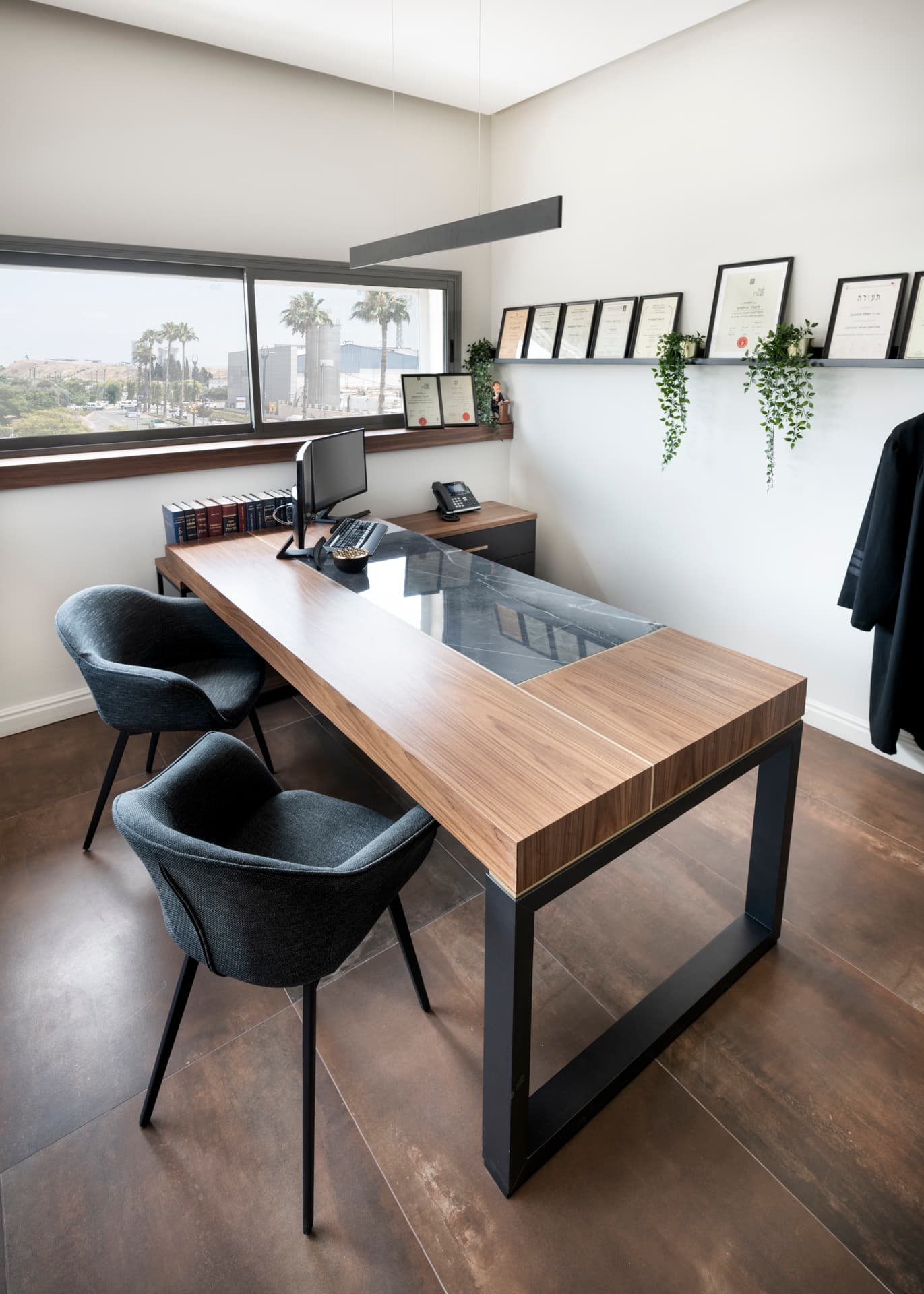 L-shaped walnut desk with an inset dark stone panel on a black steel base beside a corner window in the private office of Othman Office 2