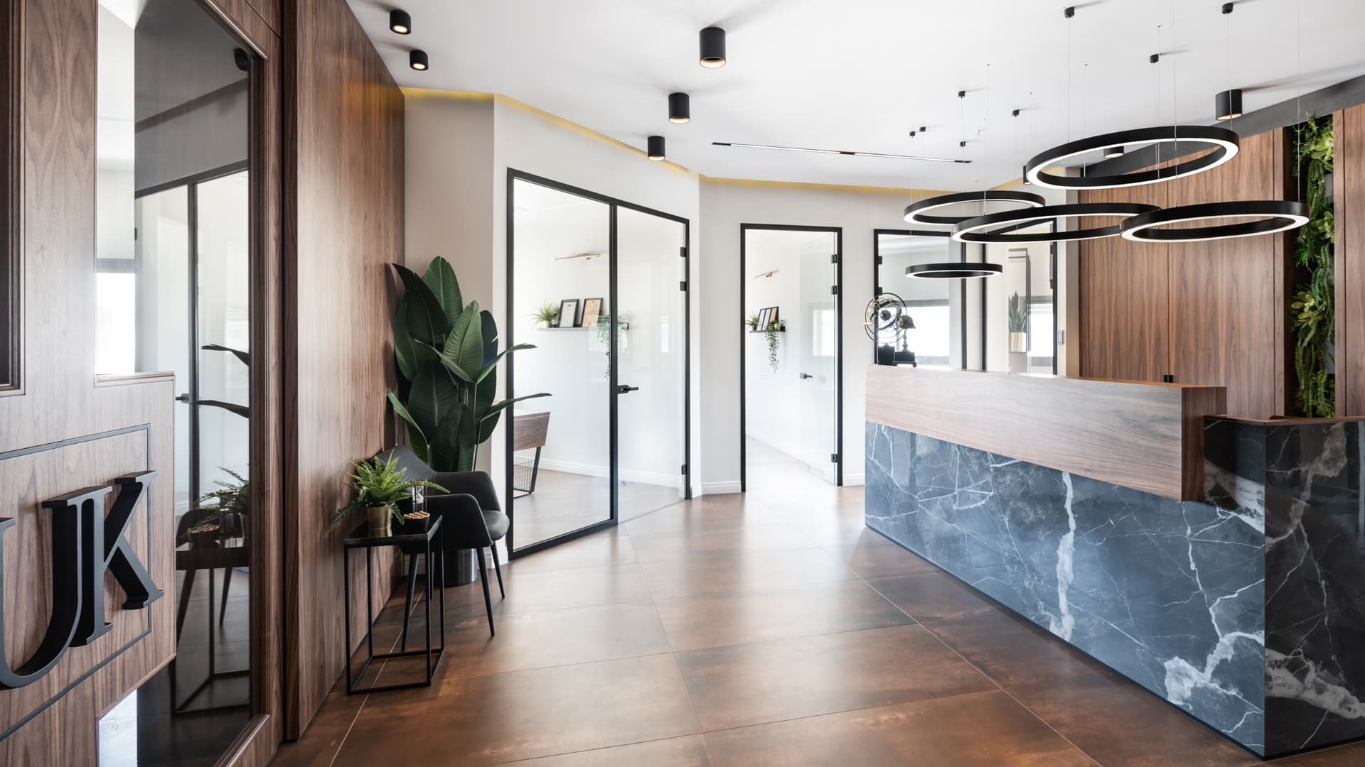 Angled view along the reception desk, with black-framed glass doors, walnut panelling and ring pendants in the reception of Othman Office 2