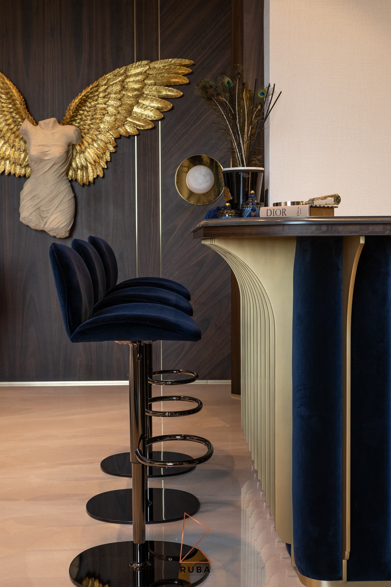 Navy velvet bar stool beside the brass-finned counter with a winged sculpture on a walnut wall in the bar of Patagonia