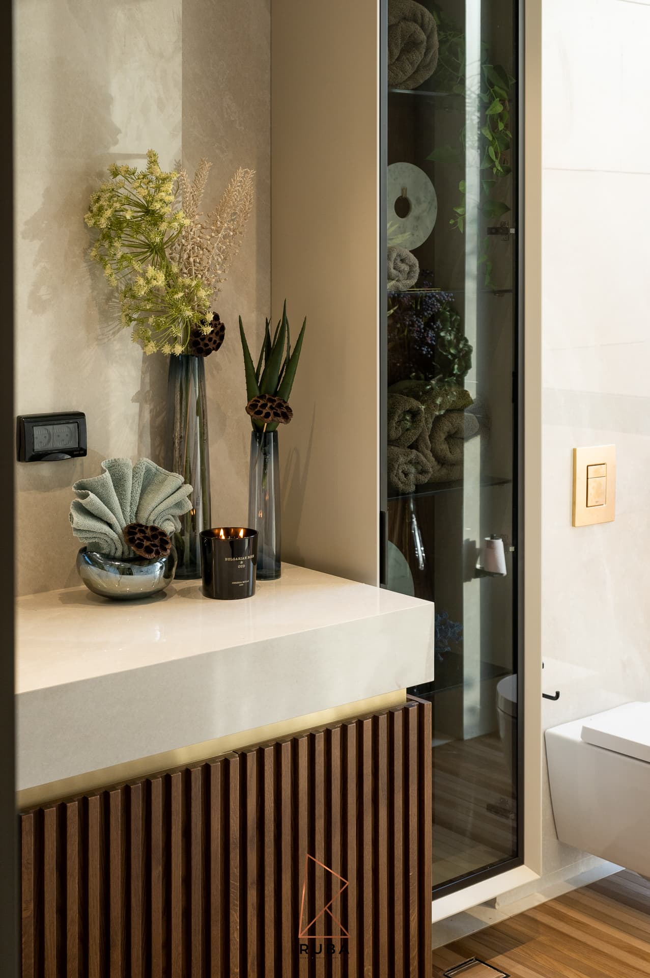 Stone vanity with a ribbed wood front, shell dish and slim vases beside a glass cabinet in the powder bathroom of Patagonia