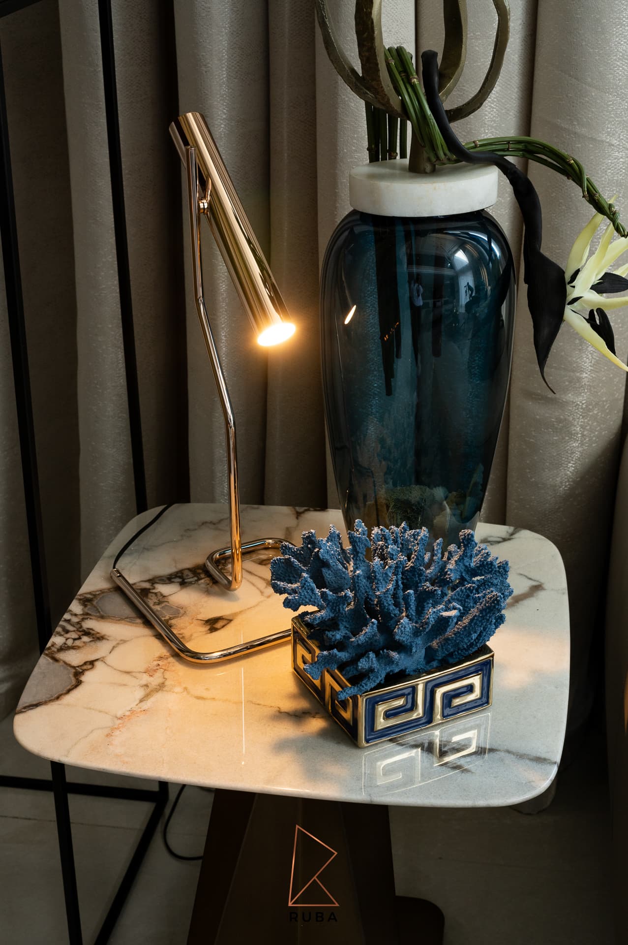 Brass task lamp and blue coral accent on a veined marble side table beside curtains in the living room of Patagonia