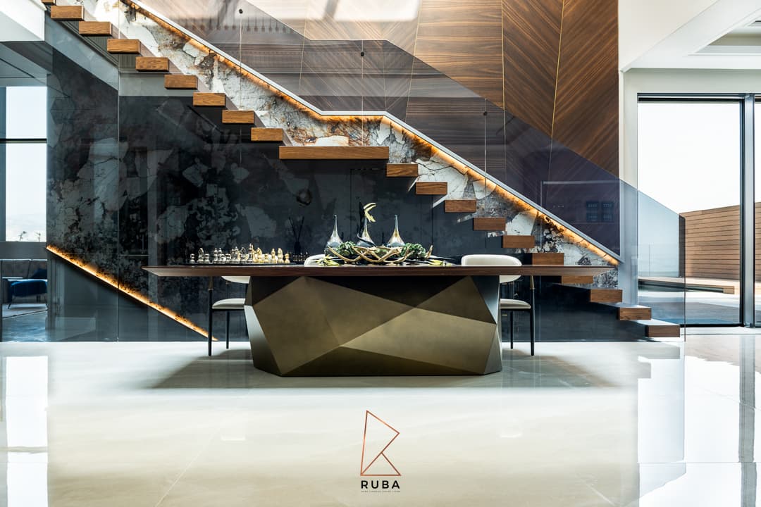 Dining table on a faceted bronze base beneath a floating walnut staircase with a backlit veined stone stringer in Patagonia