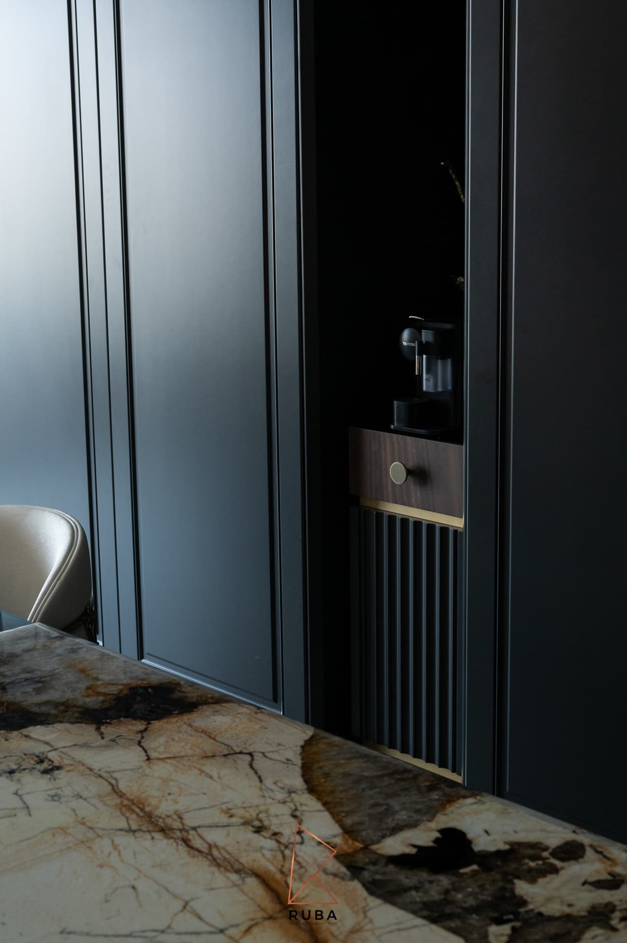 Veined stone table edge in front of black panelled cabinetry with a lit walnut niche in the dining room of Patagonia
