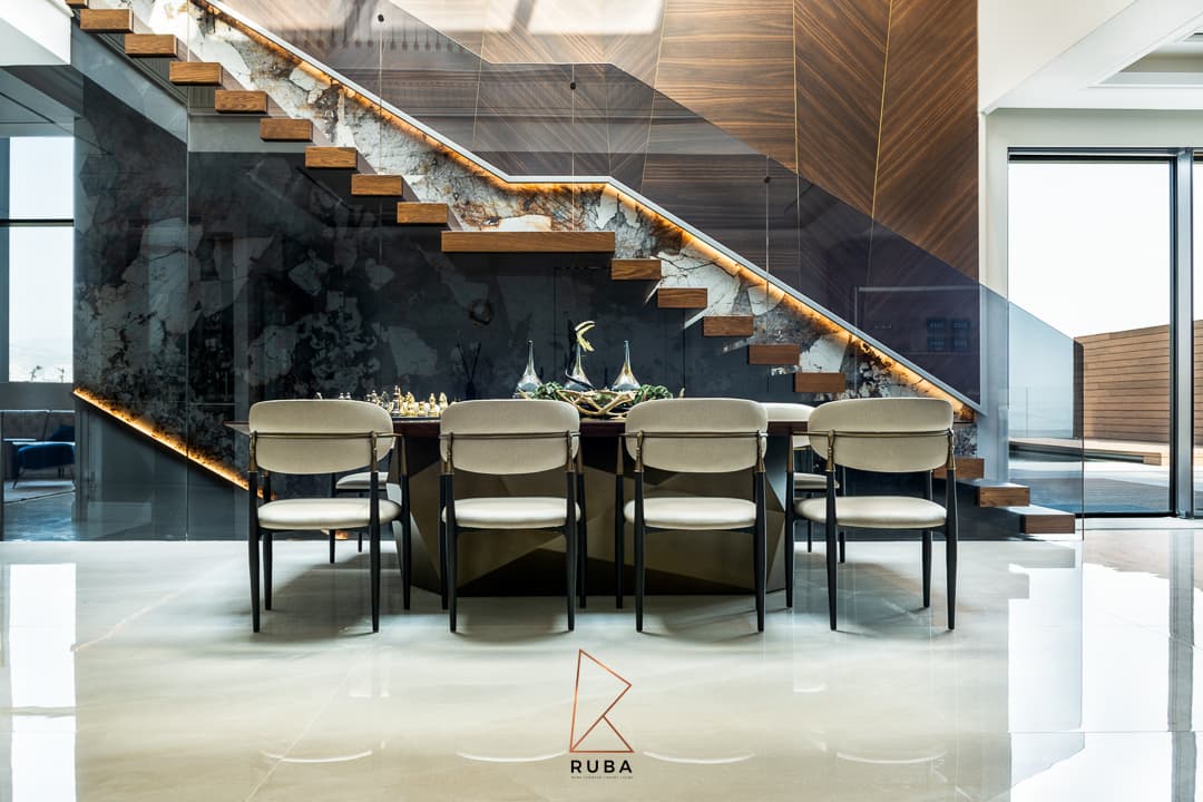 Row of cream upholstered dining chairs under the floating staircase with its backlit stone stringer in Patagonia