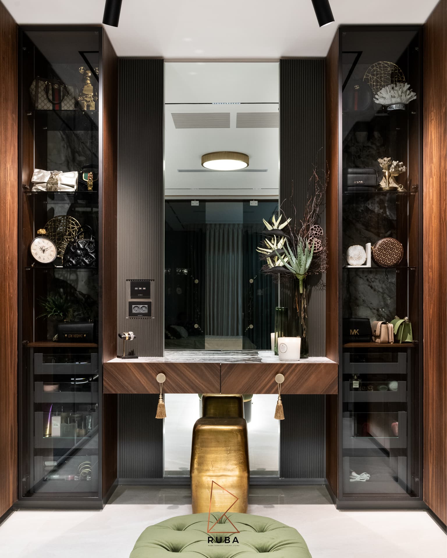 Dressing table between lit glass display cabinets with a brass stool and walnut drawers in the dressing room of Patagonia