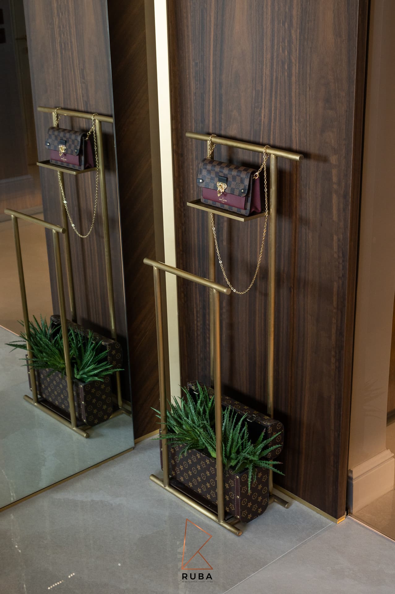 Brass valet stands mounted against a walnut wall, reflected in a tall mirror, in the dressing room of Patagonia