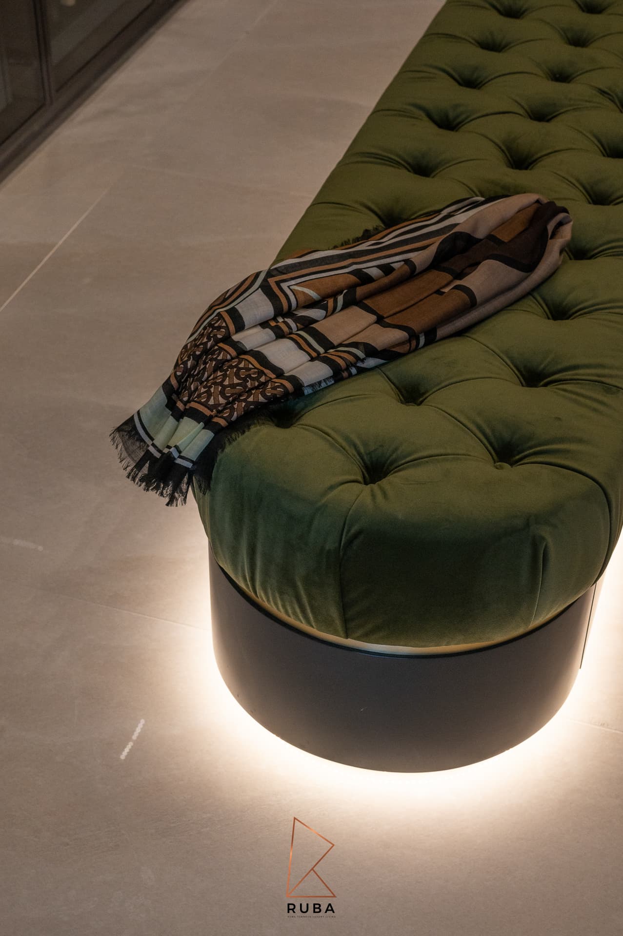 Green tufted velvet bench on a softly lit black plinth with a draped scarf in the dressing room of Patagonia
