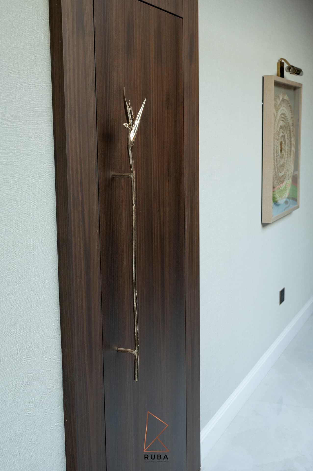 Walnut door with a sculpted brass branch pull beside a framed textural artwork in the entrance of Patagonia