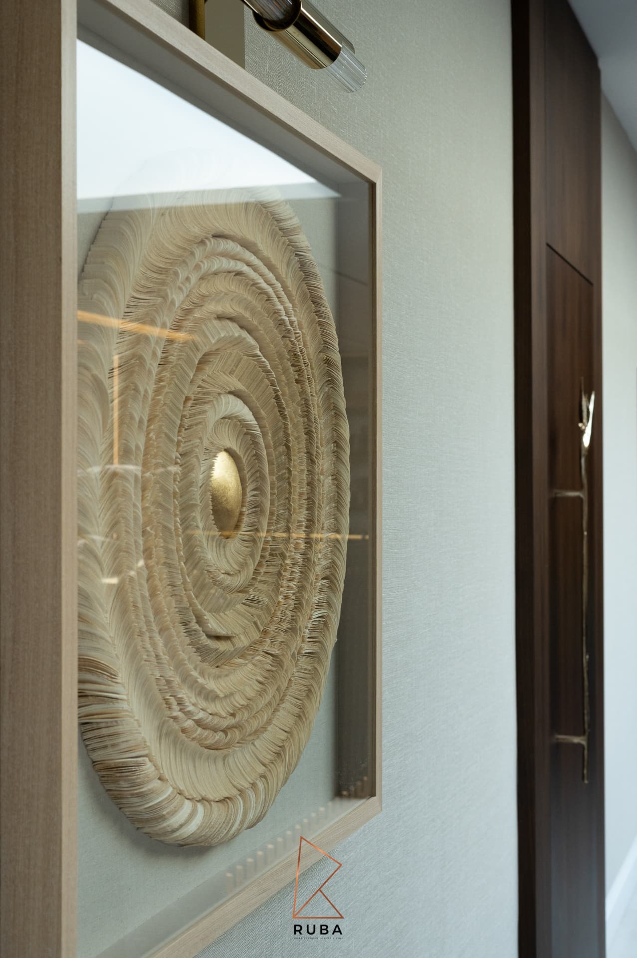 Framed circular feather-textured artwork with a brass picture light in the entrance of Patagonia