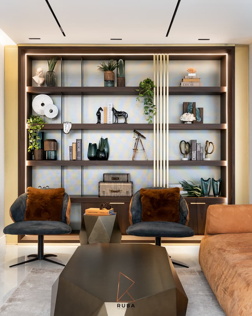 Family room with backlit walnut shelving, brass slat accents, swivel lounge chairs and a faceted table in Patagonia