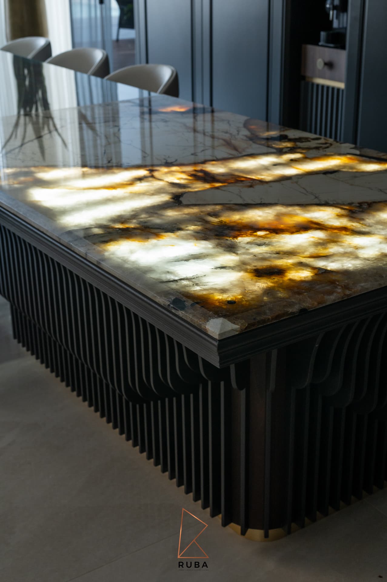 Backlit veined stone countertop glowing amber above a fluted black island base in the kitchen of Patagonia
