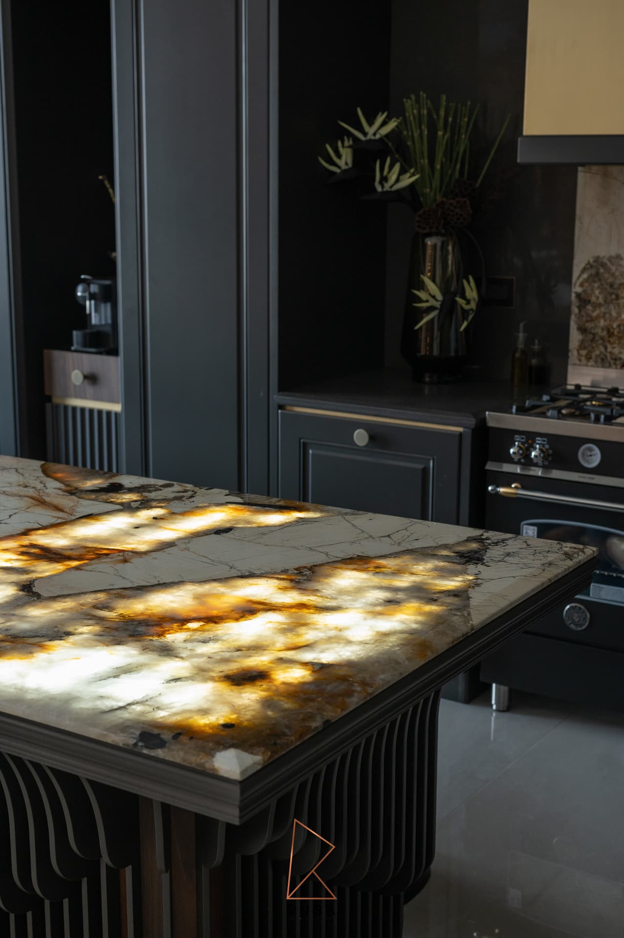 Corner of the backlit stone island in front of black cabinetry and a range in the kitchen of Patagonia