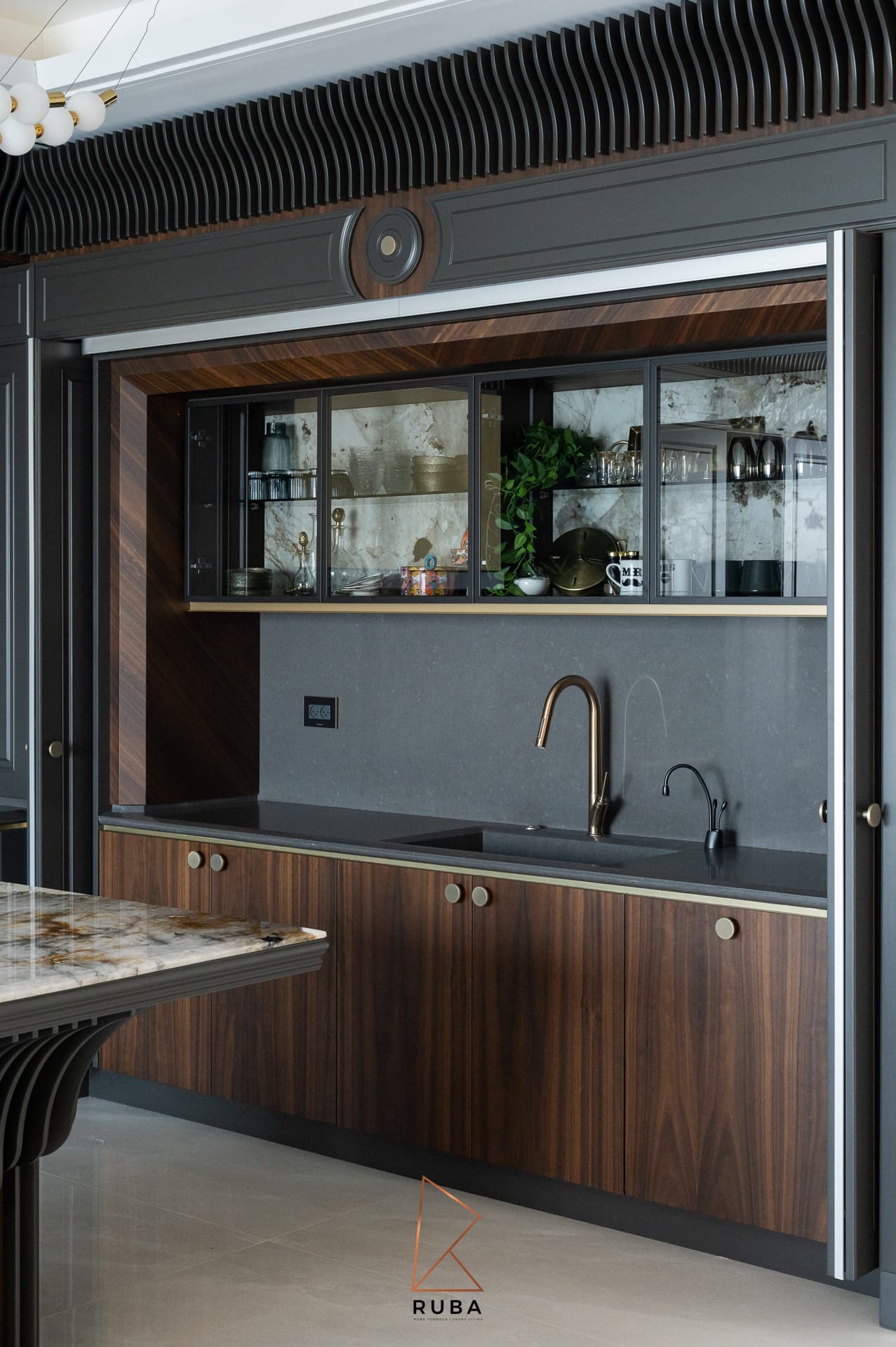 Walnut pocket-door pantry with a dark stone counter, copper faucet and glass wall cabinets in the kitchen of Patagonia