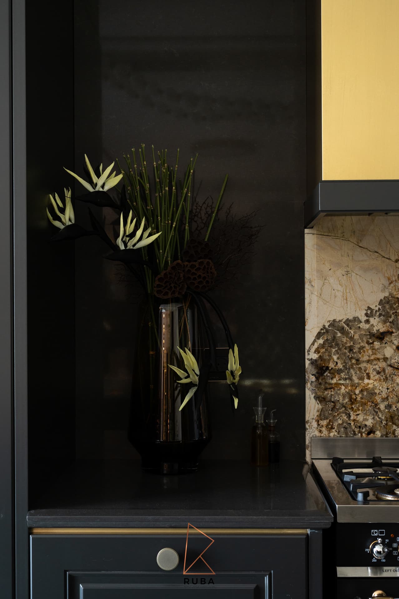 Tall smoked glass vase with pale blooms on a black counter beside the brass range hood in the kitchen of Patagonia