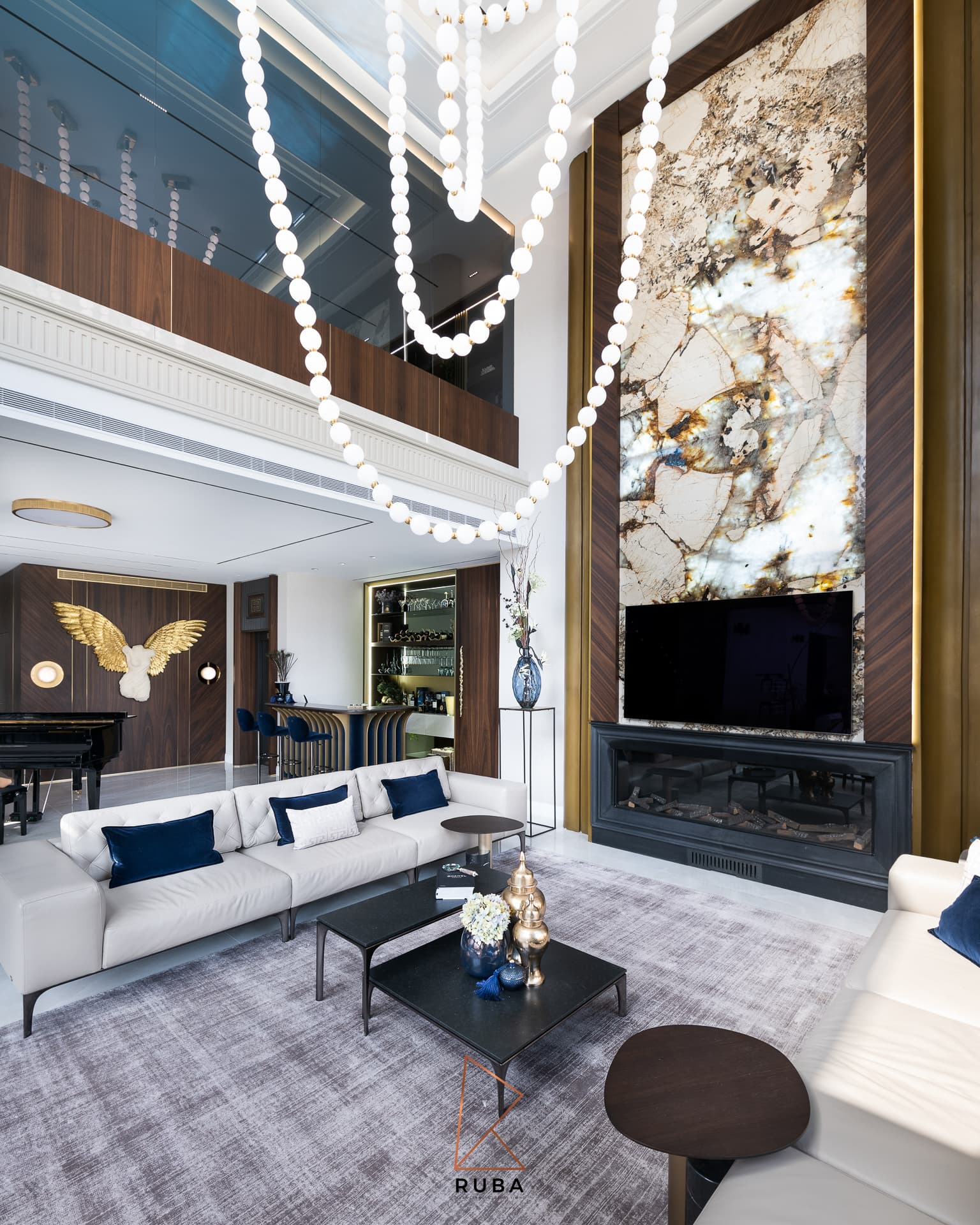Angled view of the double-height living room with a backlit veined stone wall and cascading beaded pendant in Patagonia