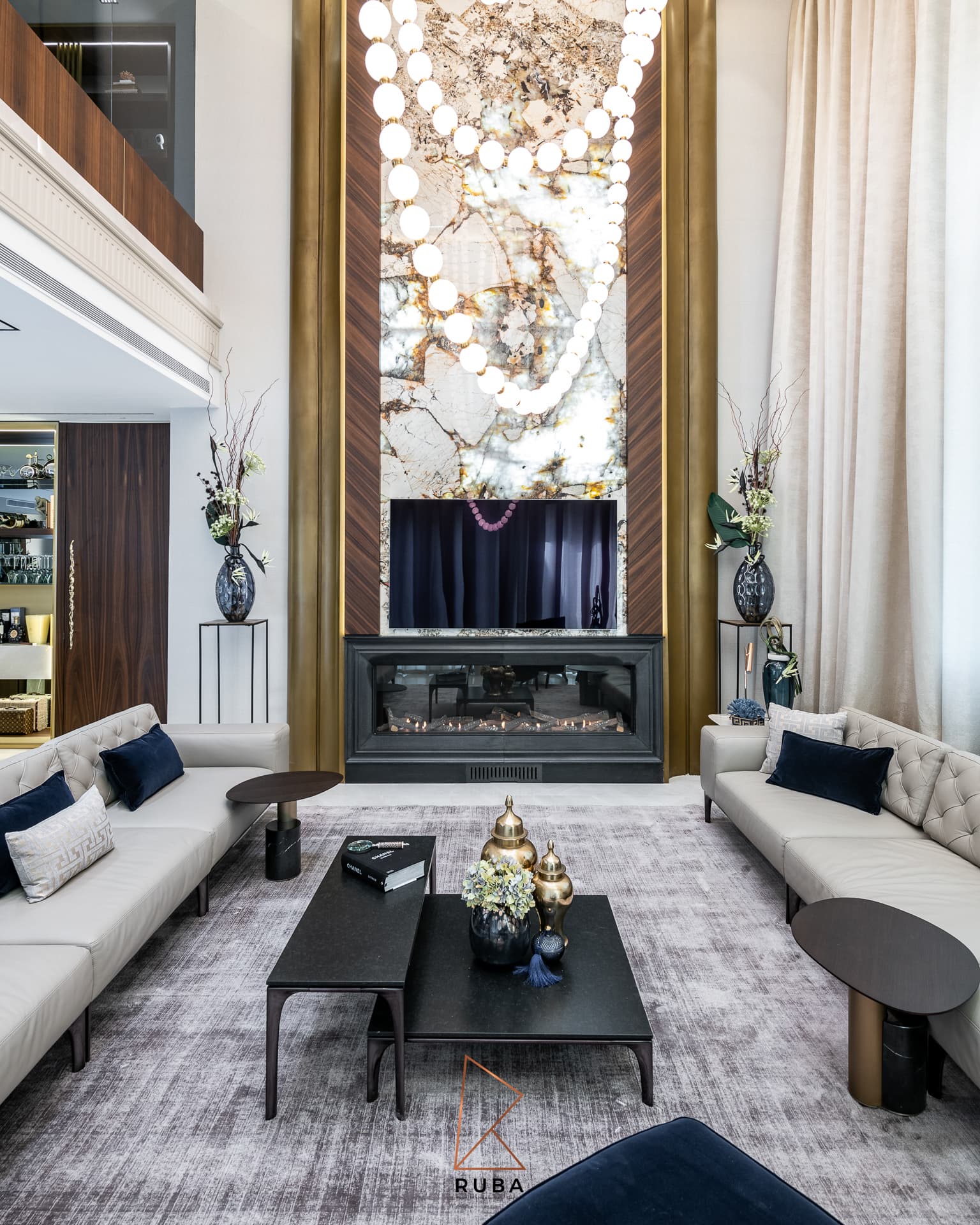 Symmetrical fireplace wall of backlit veined stone framed in walnut and brass, facing white sofas, in the living room of Patagonia