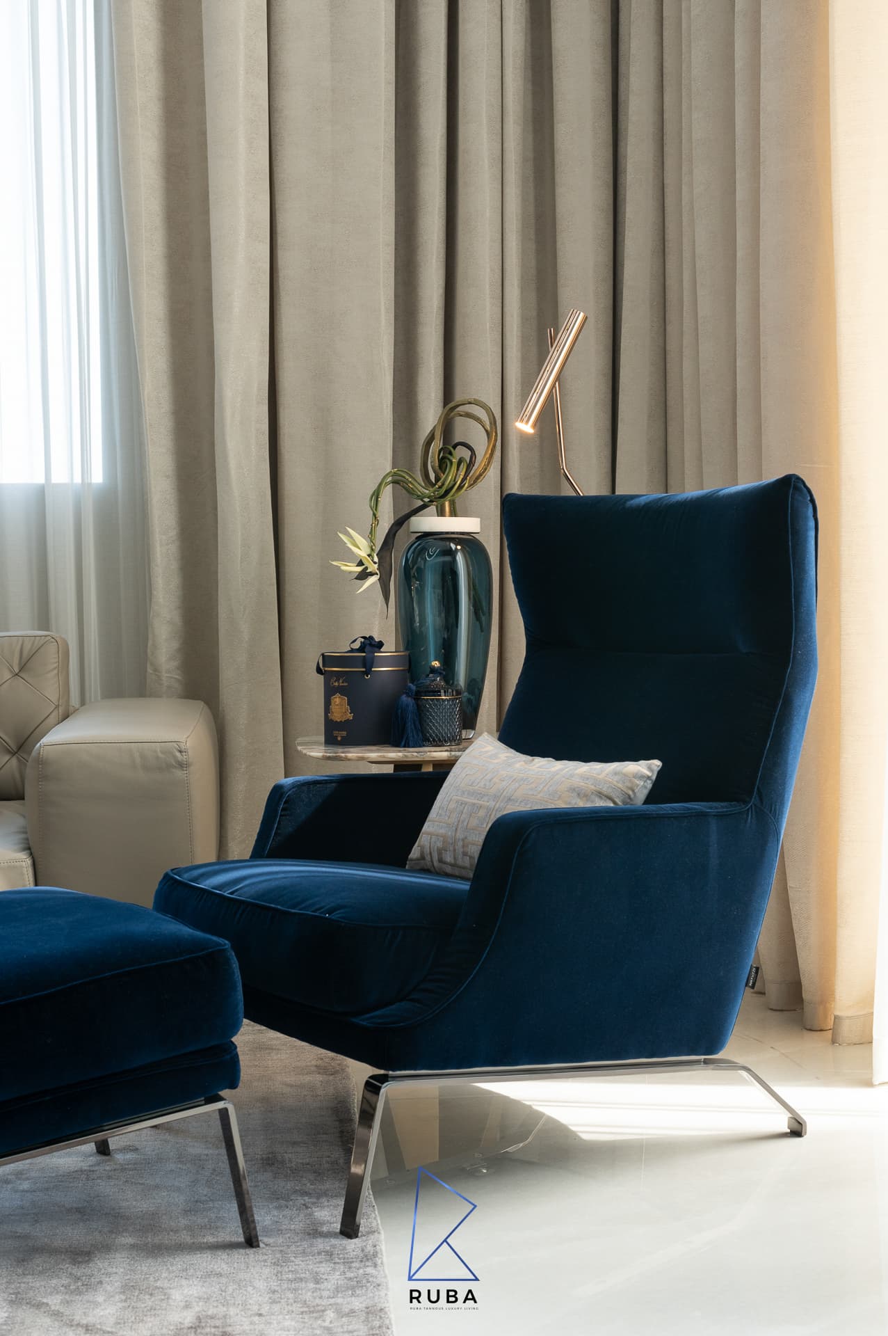Navy velvet wingback armchair and ottoman beside beige curtains and a slim brass lamp in the living room of Patagonia