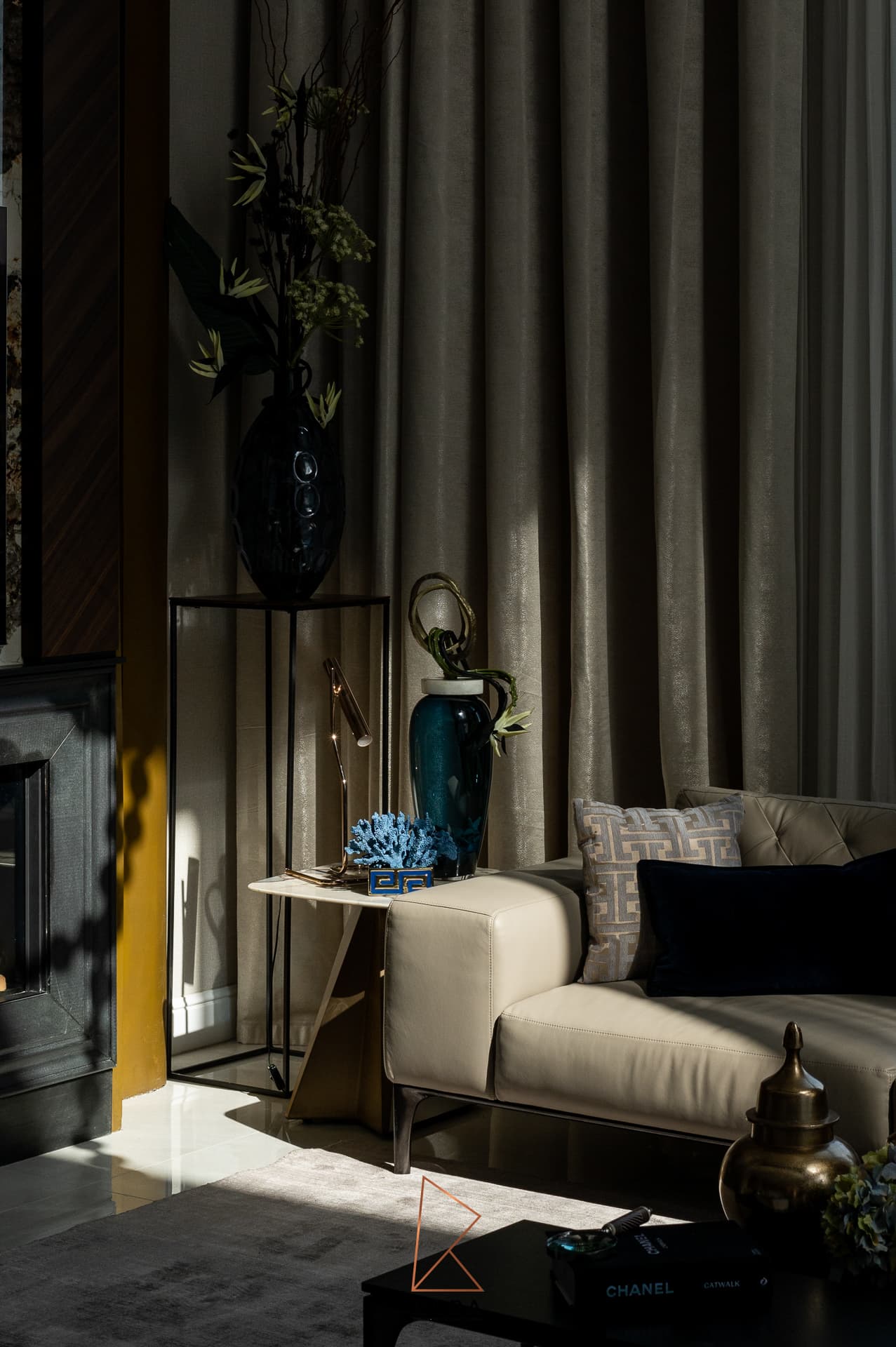 Shadowed corner of the living room with a leather sofa, teal glass vase and brass side lamp against heavy curtains in Patagonia