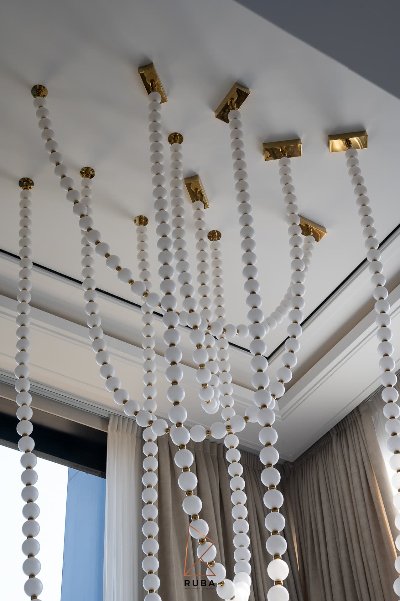 White glass bead pendant strands hanging from brass ceiling mounts in the double-height living room of Patagonia