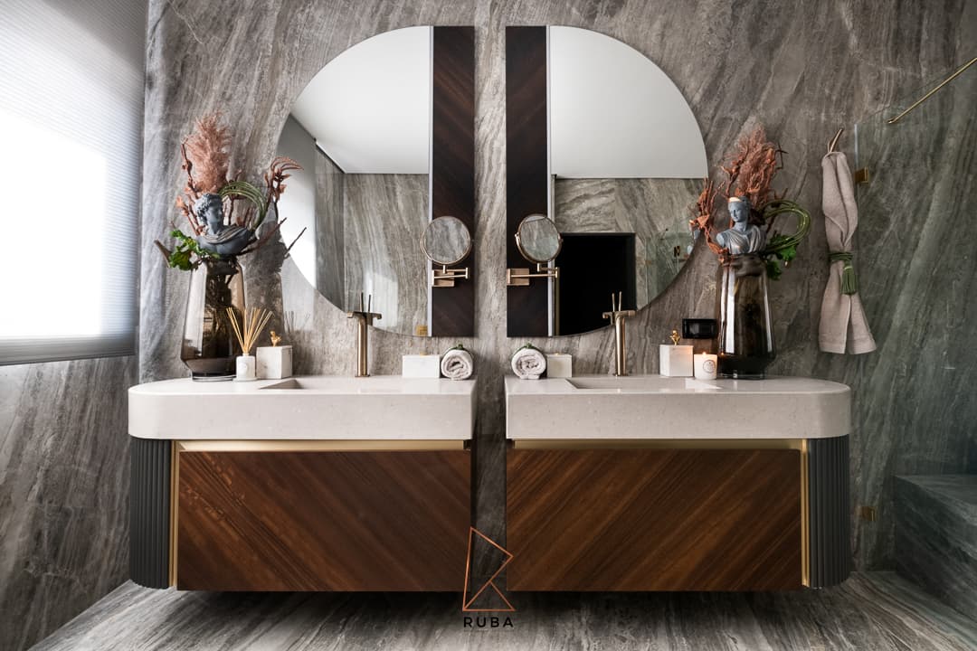 Double vanity with a split round mirror, diagonal walnut drawers and grey veined stone walls in the master bathroom of Patagonia