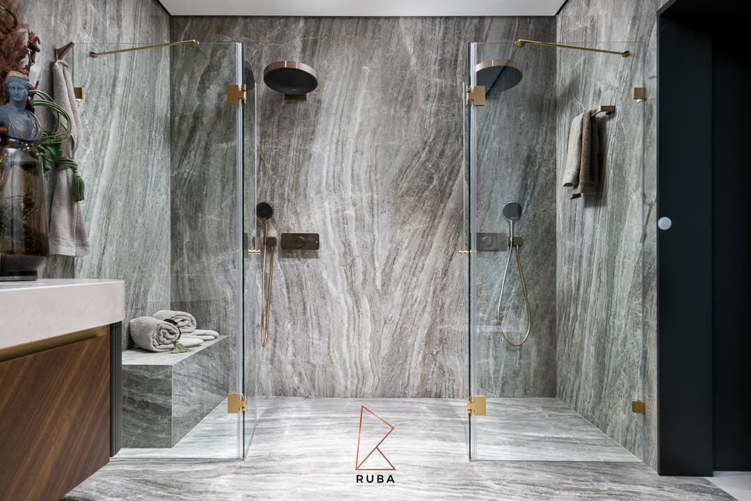 Twin glass walk-in showers with brushed brass rain heads against grey veined stone in the master bathroom of Patagonia
