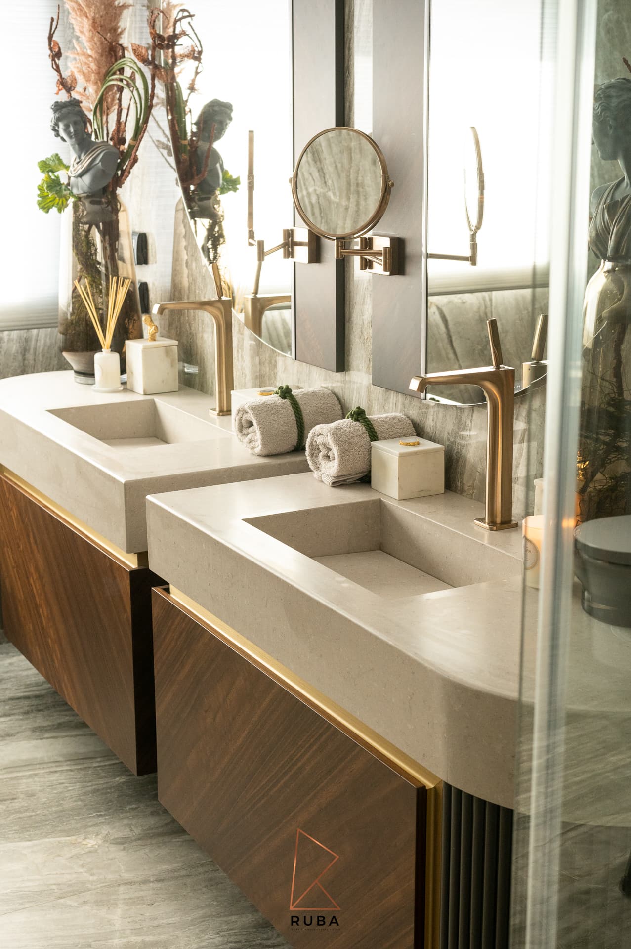 Two stone vanities with brass faucets and extendable shaving mirrors seen past a glass panel in the master bathroom of Patagonia