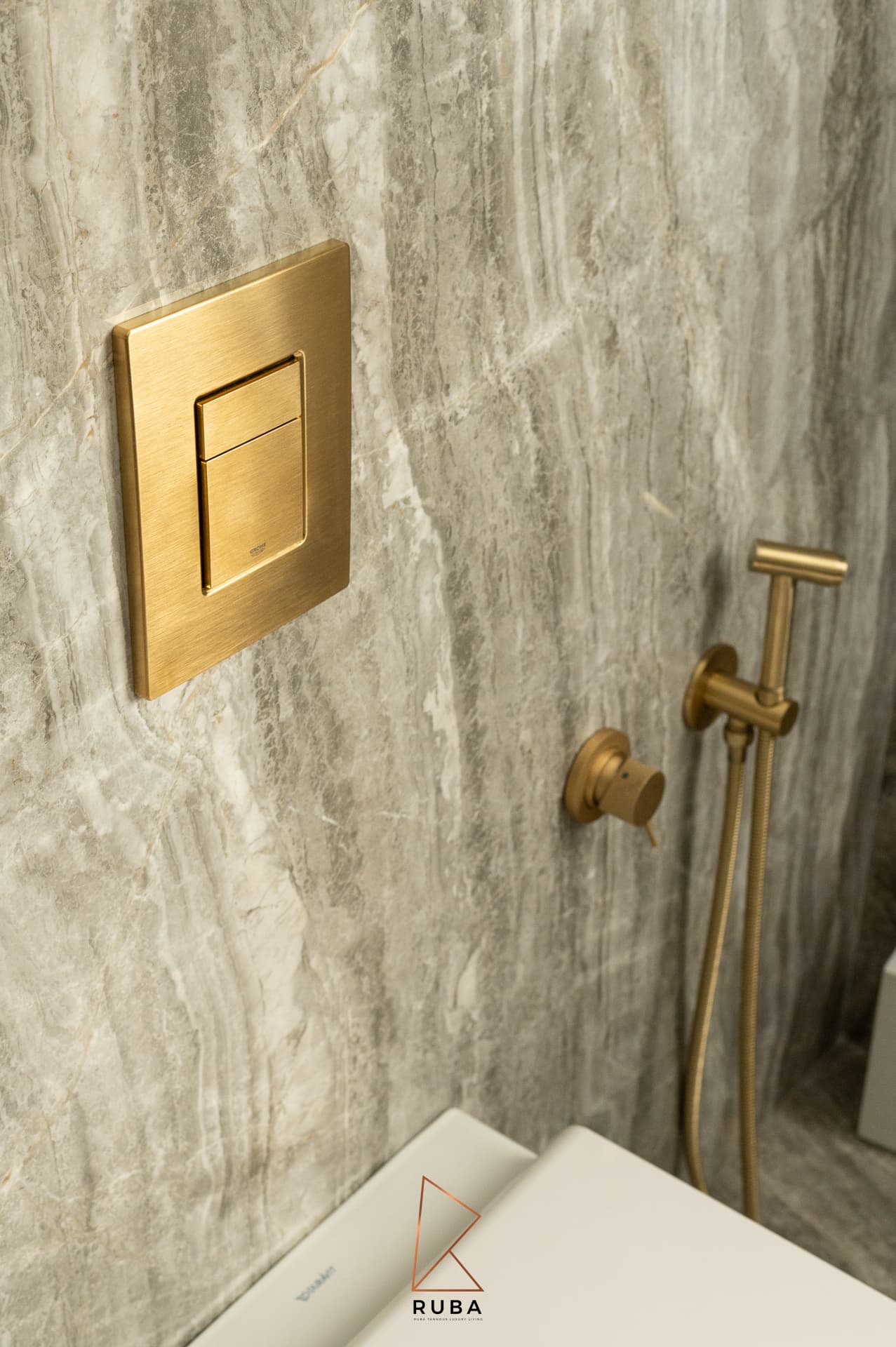 Brushed brass flush plate and bidet spray mounted on grey veined stone in the master bathroom of Patagonia