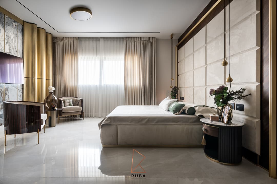 Master bedroom with a padded panel headboard wall, fluted brass column feature and velvet lounge chairs in Patagonia