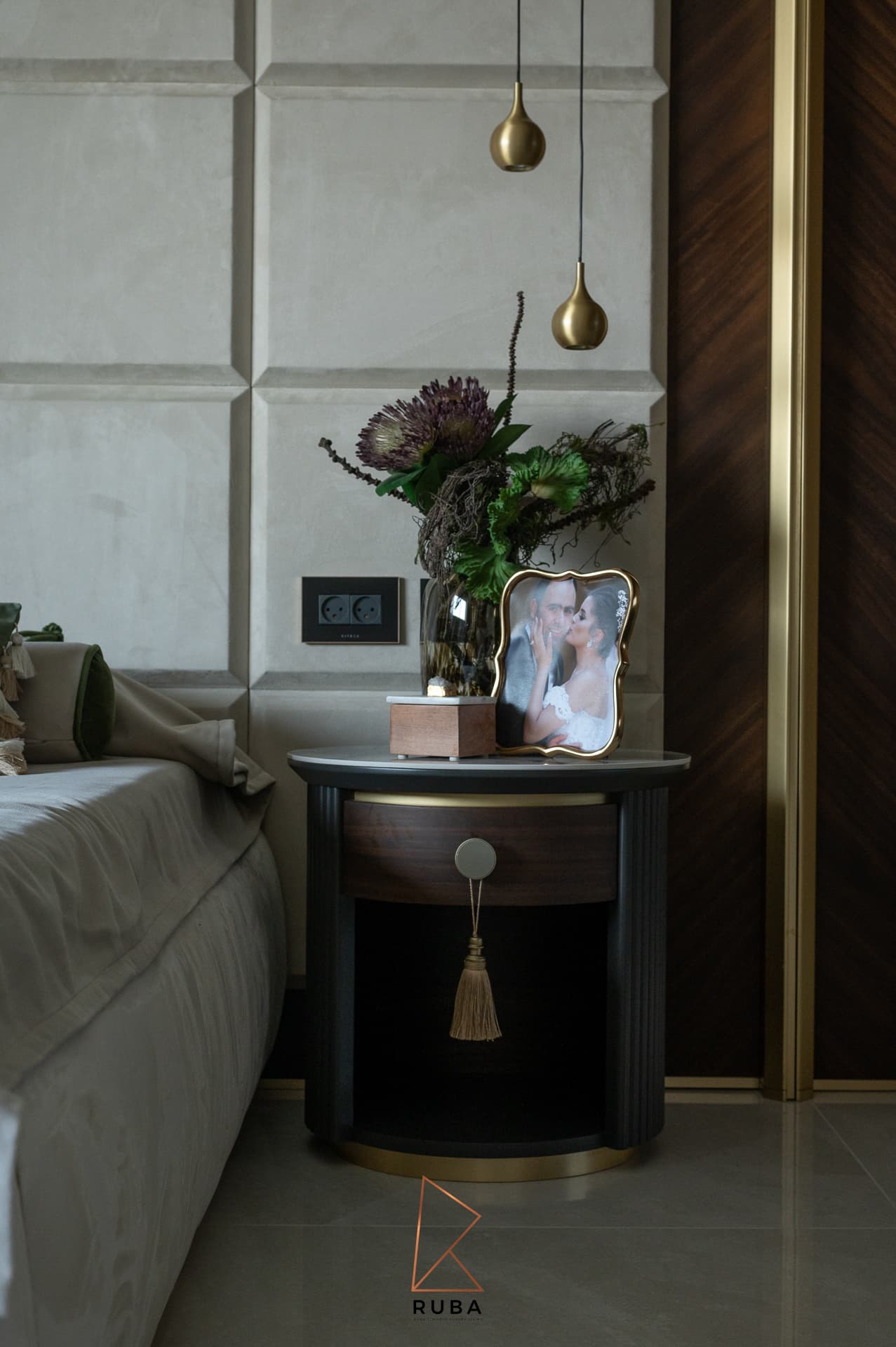 Nightstand with a brass tassel pull and protea stems beside a brass-trimmed walnut wardrobe panel in the master bedroom of Patagonia