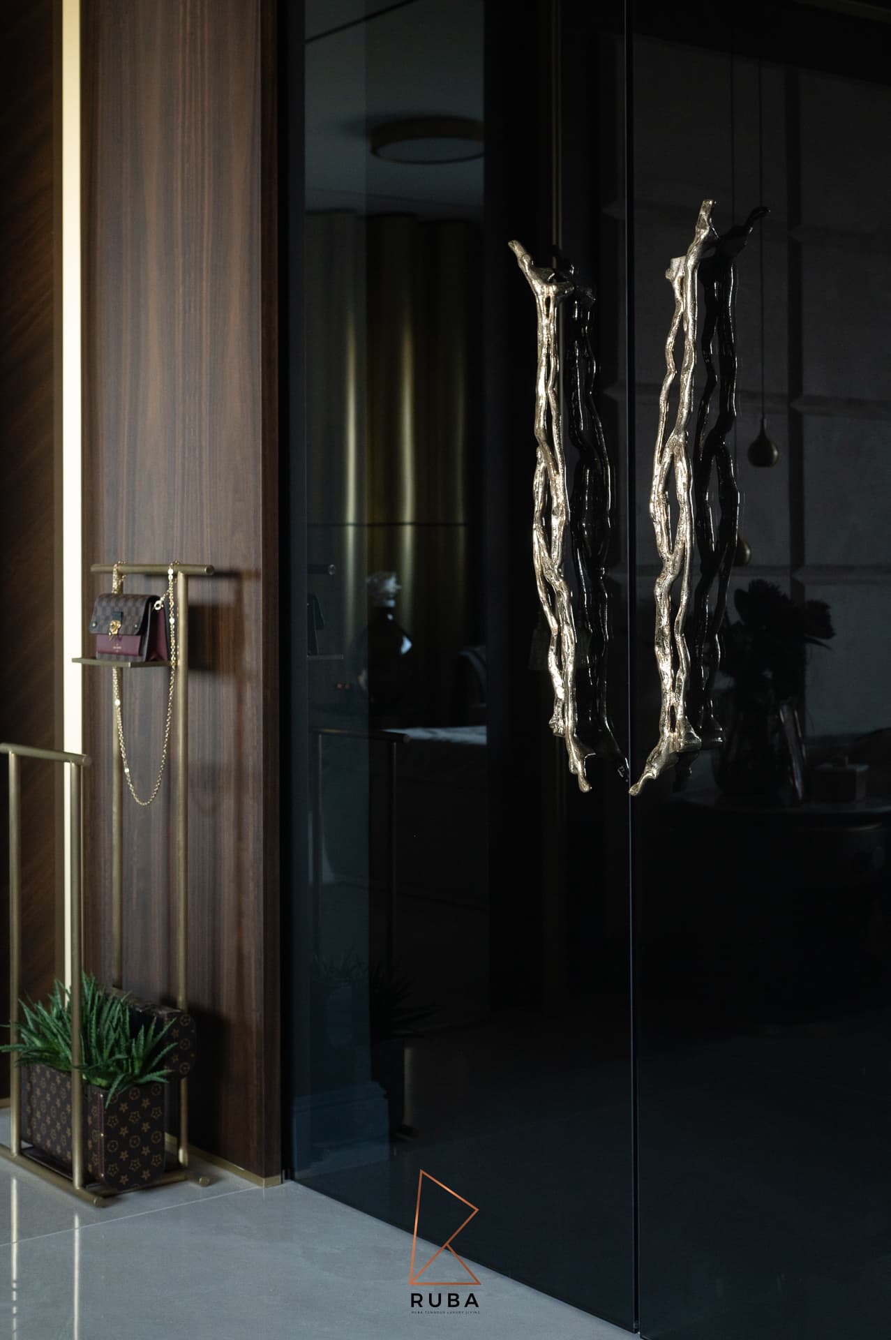Black glass wardrobe doors with sculpted brass branch-shaped pulls beside a walnut wall in the master bedroom of Patagonia