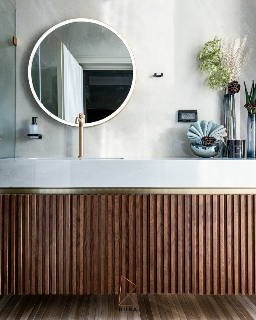 Round backlit mirror above a stone vanity with a vertical ribbed wood front and brass faucet in the powder bathroom of Patagonia
