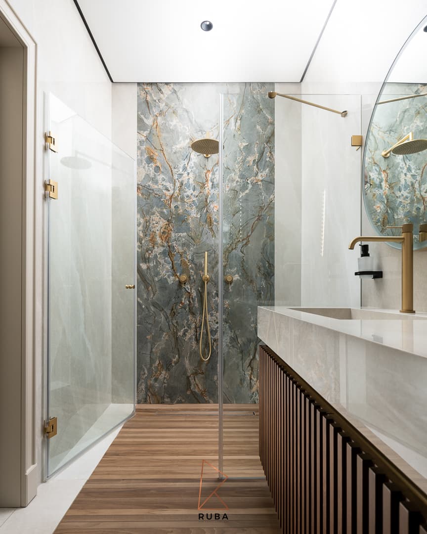 Glass shower with a blue-green veined stone wall, brass rain head and wood floor in the powder bathroom of Patagonia