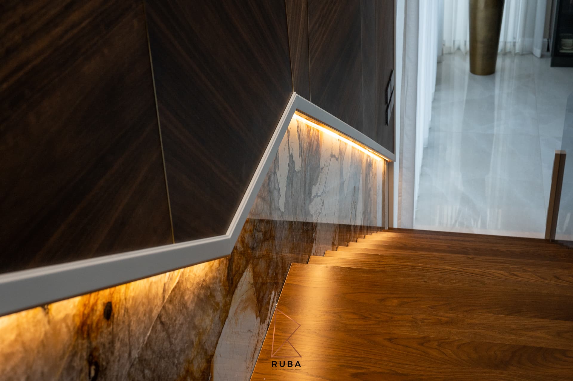 Walnut stair treads beside a backlit veined stone stringer and a chevron walnut wall on the staircase of Patagonia