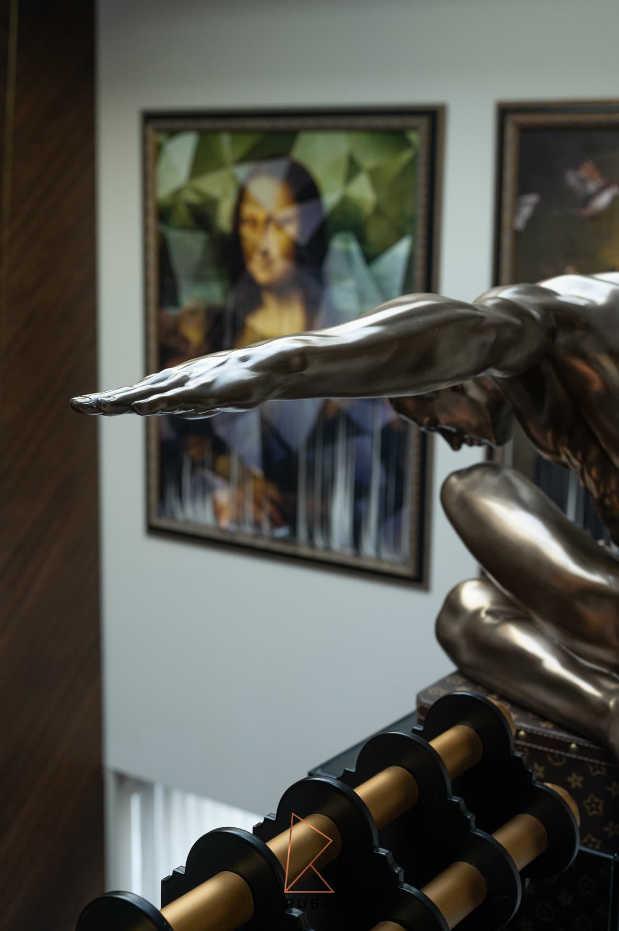 Close view of the bronze sculpture's outstretched arm with a framed painting beyond on the staircase landing of Patagonia